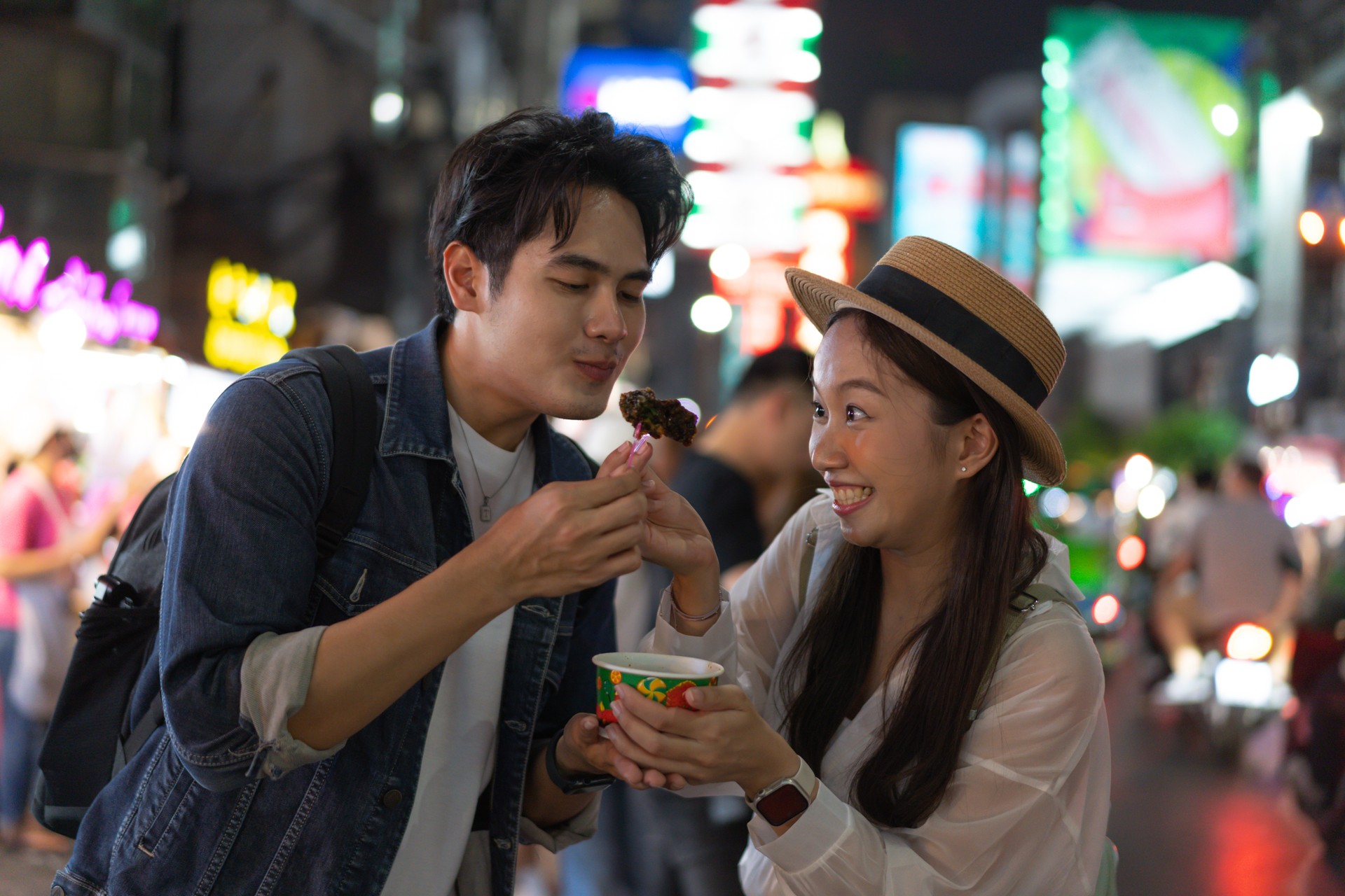 Asian couple tourist backpacker enjoying and eating street food in night market with crowd of people at Yaowarat road, Bangkok