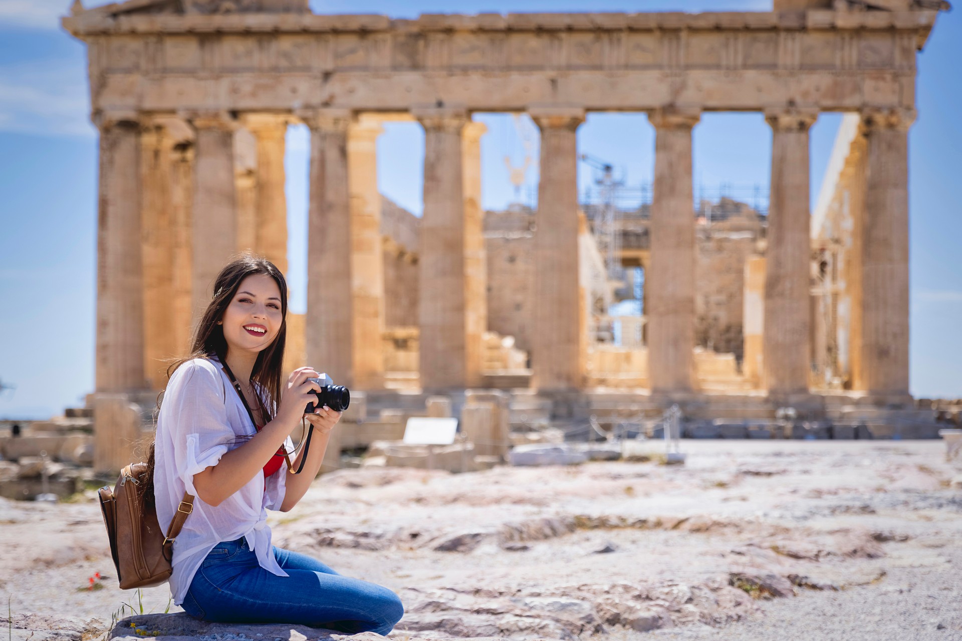 A young woman taking pictures of the Parthenon Temple at the Acropolis of Athens