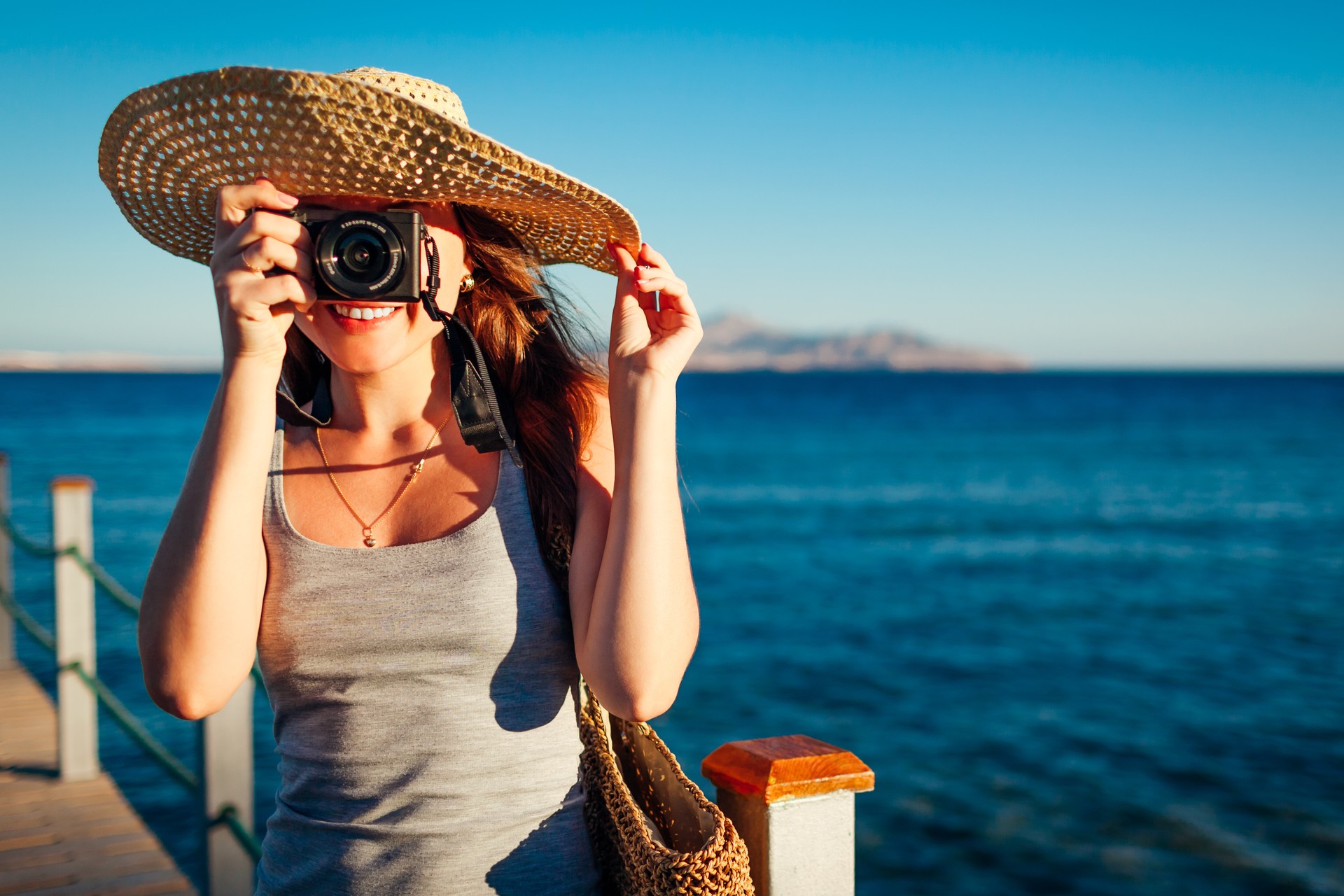 Young woman traveler taking photos of sea landscape on pier using camera. Summer vacation in Egypt